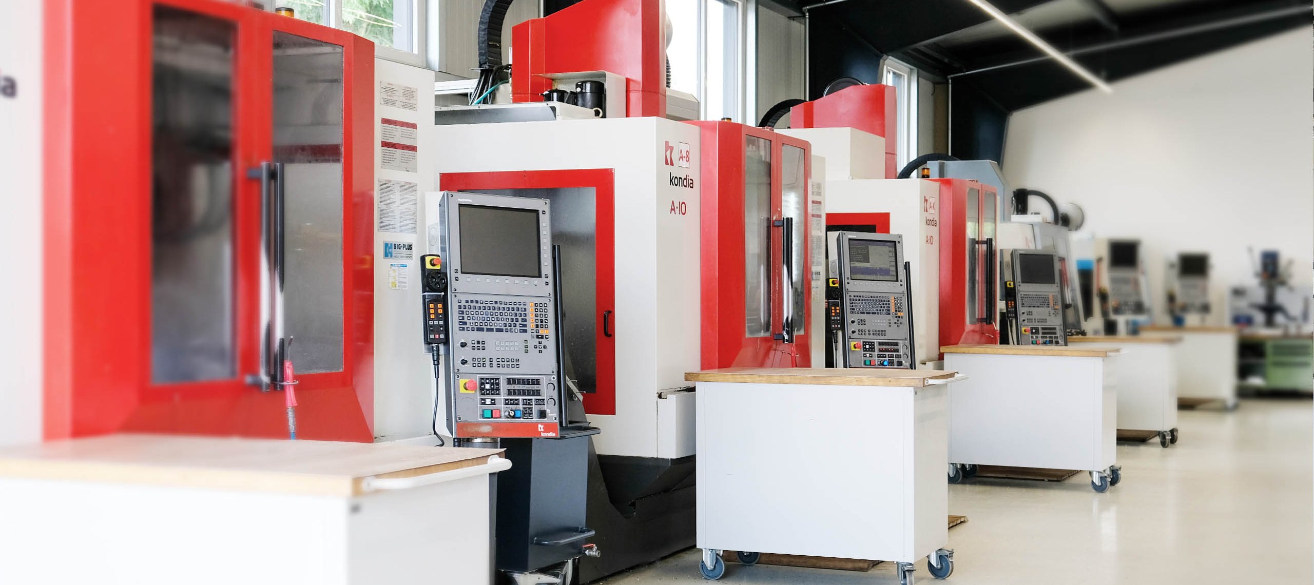 CNC ZERSPANUNG Reihe von CNC-Fräsmaschinen mit Steuerpulten in einer Werkstatt, links Text 'CNC ZERSPANUNG' und 'WU Mechanische Werkstätte'.