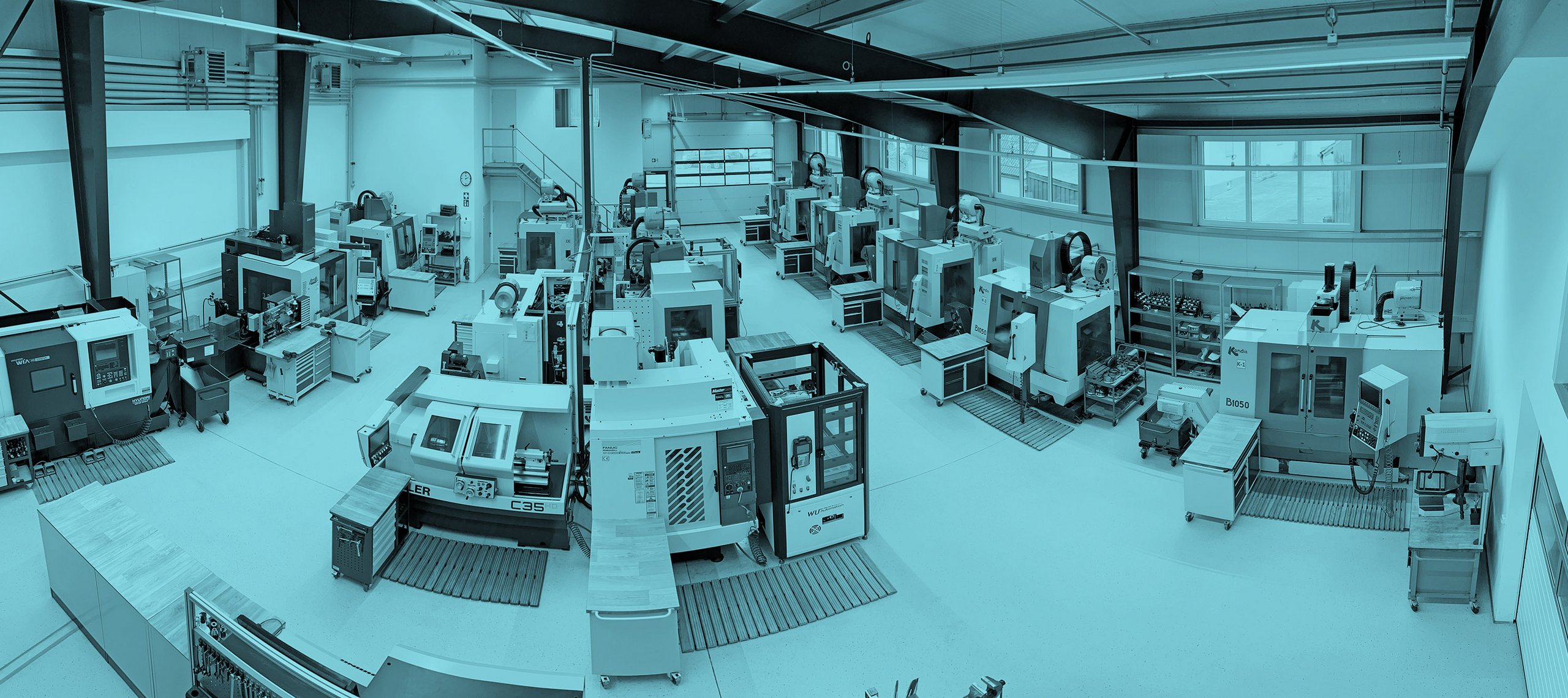 CNC Zerspanung, WU Systems Blick in eine Werkhalle mit mehreren CNC-Fräsmaschinen in Reihen, Arbeitsplätze mit blauen Schubladenschränken, helle Wände und große Fenster.